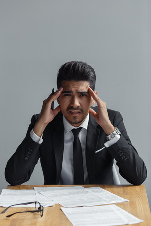 Depressed businessman sitting at the table with documents, looking at cameraの写真素材