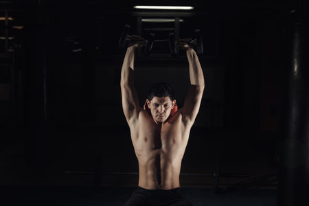 Muscular man training his shoulders with dumbbells