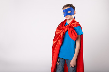 Super hero boy in red cape and blue mask posing in studio.の写真素材