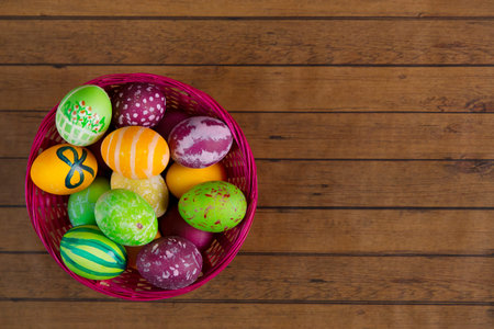 Easter colorful eggs in basket on wooden background, top view