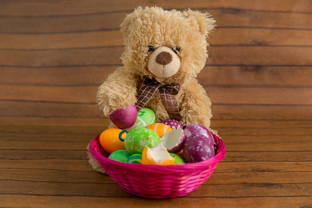 Easter colorful eggs in basket and fluffy toy bear on wooden background. April religion holiday decorationの写真素材