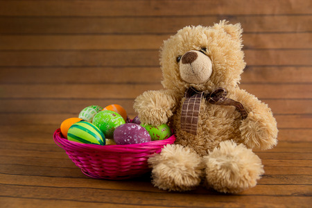 Easter color painted eggs in basket and teddy bear on wooden background. April religion holiday decorationの写真素材