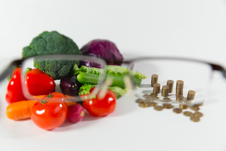 Lack of money on food, small pension and no vegetables, low social status of older people concept. Fresh ripe vegetable composition against a stack of coins, view through the glassesの写真素材