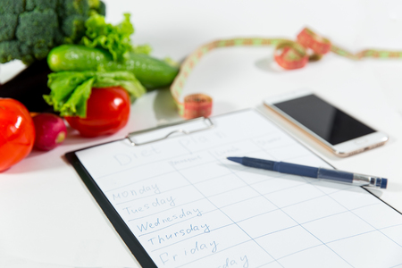 Vegetables, measuring tape, mobile phone and notebook with diet plan isolated on white background, top view. Nutritionist doctor workspace conceptの写真素材