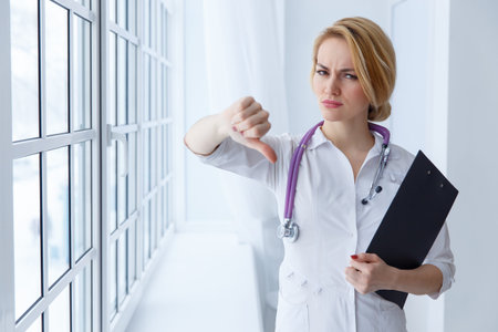 Closeup portrait, doctor woman, giving thumbs down gesture looking with negative expression, disapproval. Unhappy female health care professional. Emotion facial expression.の写真素材
