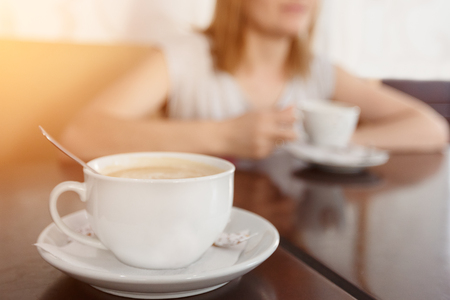 Selective focus on a cup with aromatic coffee. Blurred background with girl drinking coffee cup.の写真素材