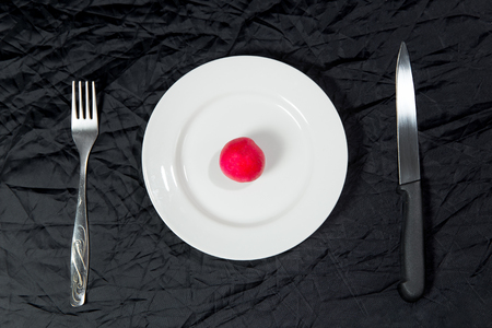 One red radish on white plate on black background with fork and knife. top viewの写真素材