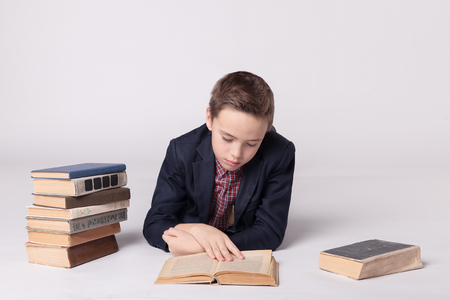 Cute boy in a suit lies and reading a book on a white background.の写真素材
