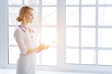 Beautiful female doctor while filling up medical application form with sunlightの写真素材