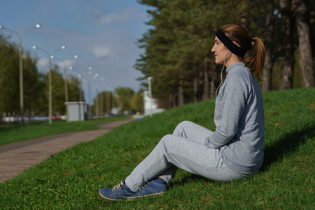 Fitness woman with smartphone sitting and listening music at city park.の写真素材