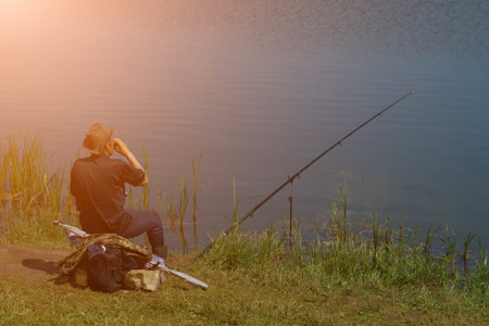 fisherman with fishing rod catching fish, sitting riverside. sunlight