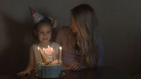 mother and daughter blow out candles on a birthday cake and making a wish. the birthday of a little...