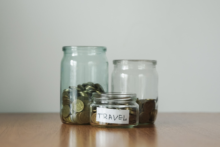 Coins in glass jars for different needs, money boxes. Distribution of cash savings concept. Travel sticker.の写真素材
