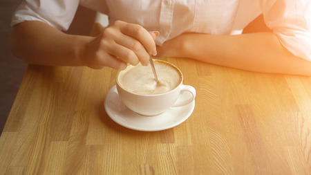Hand of girl stiring sugar in coffee close up, sunlightの写真素材