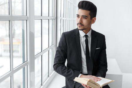 Young handsome businessman in black suit sitting and reading book. concept educationの写真素材