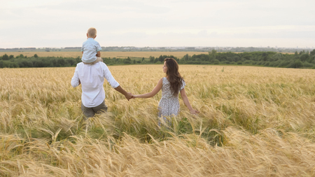 Happy childhood, family walking on the wheat field. Mother, father and little son leisures together outdoor. Parents and kid playing on summer meadowの写真素材