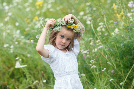 Little girl in beautiful white dress and wreath from wildflowers walking on a meadow. Cute girl and summer flowersの写真素材