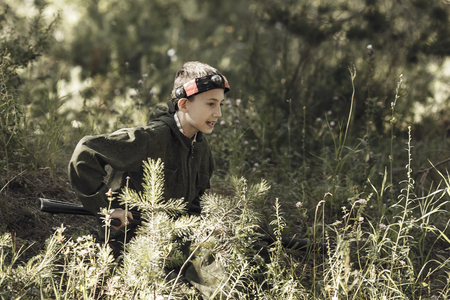 Child in camouflage with a gun shoots, laser tag in the forest. Lasertag shooting game, tonedの写真素材