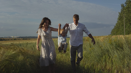 Happy family walking on summer meadow, parents playing with little son. Mother, father and child leisures together outdoorの写真素材