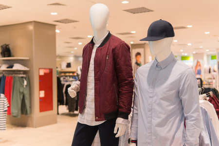 Male mannequins in red jacket, gray shirt and black baseball cap. Fashion store interior on...