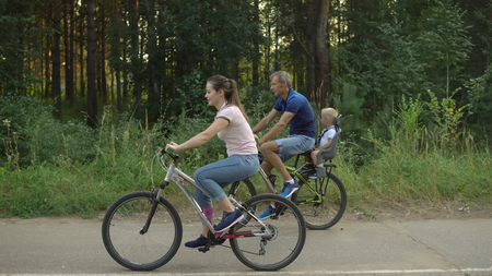 Happy family rides on bicycles in the forest. Couple with child walks on bikes in park, cycling leisureの写真素材