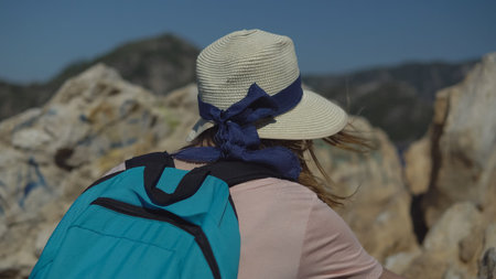 Rear view - tourist girl in hat and with backpack walking along the trail among beautiful nature....