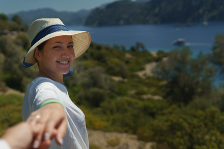 Portrait of cute young woman in hat holding an unknown man's hand and calling after him to enjoy the beautiful nature and the sea while on sunny summer day. copyspaceの写真素材