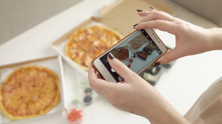 Photographing food. Hands of girl with smartphone taking picture of delicious pizzaの写真素材