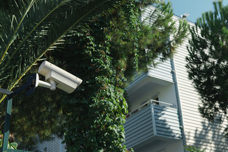 Outdoor CCTV camera in the sunny day on the background of the house with balconiesの写真素材