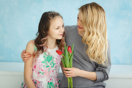 Mother and daughter with a bouquet of tulips sitting on a blue wall background.の写真素材