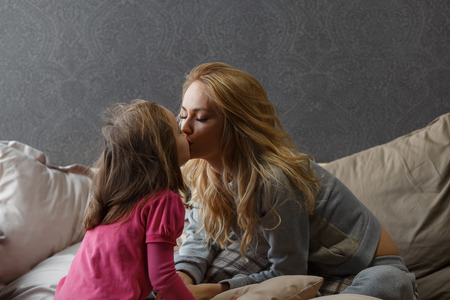 mother and little daughter are sitting on the bed and smacking.の写真素材