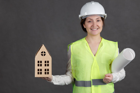 Young woman engineer in protective helmet and vest with documents and mockup in hands.の写真素材