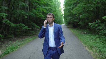 Business man in suit talking on the phone walking in the woods.の写真素材