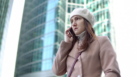 Angry young woman talking on the phone among tall buildings.の写真素材