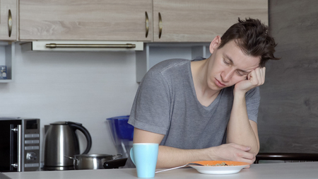 Handsome man falls asleep at the breakfast table in the kitchen.の写真素材
