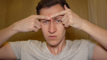 Young man tries to squeeze a pimple on his nose.の写真素材