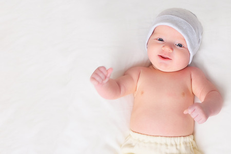 sweet baby in hat and pants smiling while lying on grey background.の写真素材