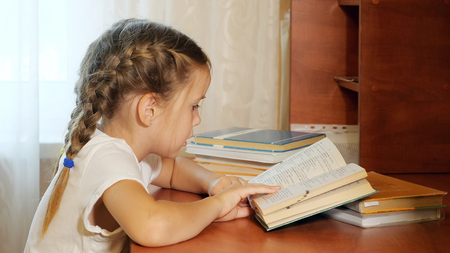 Side view of little girl with braids sitting at table and reading textbook doing homeworkの写真素材