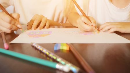 Beautiful adult woman and girl painting with pencils on paper sitting at table at home, sunlightの写真素材