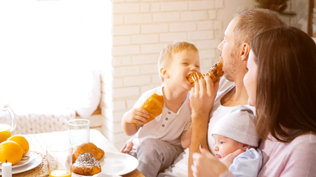 Parents with baby and funny boy smiling and while enjoying buns and juice for breakfast together, sunlightの写真素材