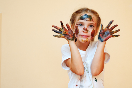 Beautiful little girl in white t-shirt showing hands with colored palms looking at cameraの写真素材