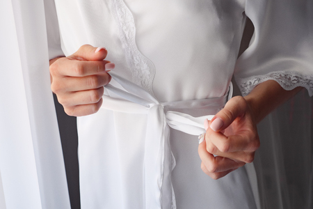 girl ties belt on her robe standing near window.の写真素材