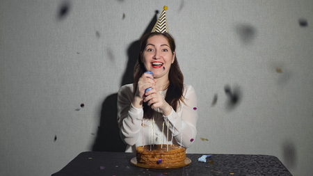 Young woman celebrates a holiday, he sits alone at a table with a cake and a candles.の写真素材