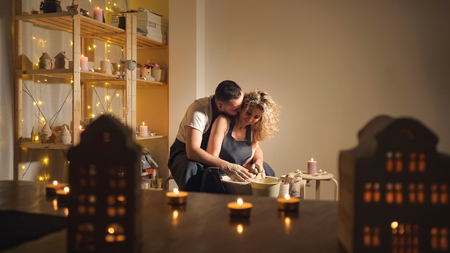 happy family on a creative joint vacation. bearded man and a young woman mold a vase in craft studio workshop.の写真素材