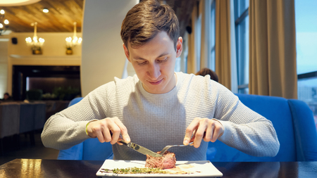 young man cutting meat beef steak eating enjoying dinner in restaurant.の写真素材