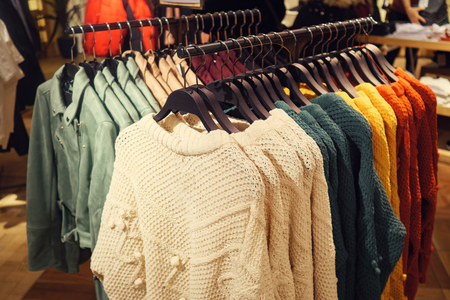 Rack with hangers of various colorful sweaters for sale in modern clothes store, tonedの写真素材