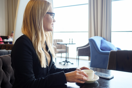 Happy girl drinking coffee, relaxing in cafe and looking at the windowの写真素材