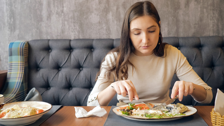 Young woman eating dinner in the restaurant. Cutting fish steak with knife and fork. Healthy eating and diet concept.の写真素材