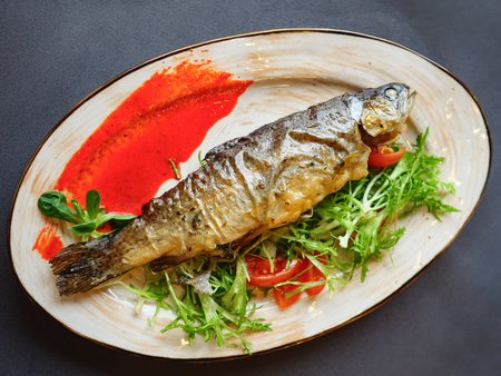Tasty baked fish in white plate on wooden table. Top viewの写真素材