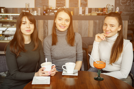 Three women girlfriends in a cafe are talking and drinking their beverages, sunlightの写真素材